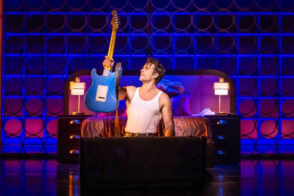 Bobby Stivic (Corey Cott) holding a blue electric guitar in "The Heart of Rock and Roll" Broadway musical